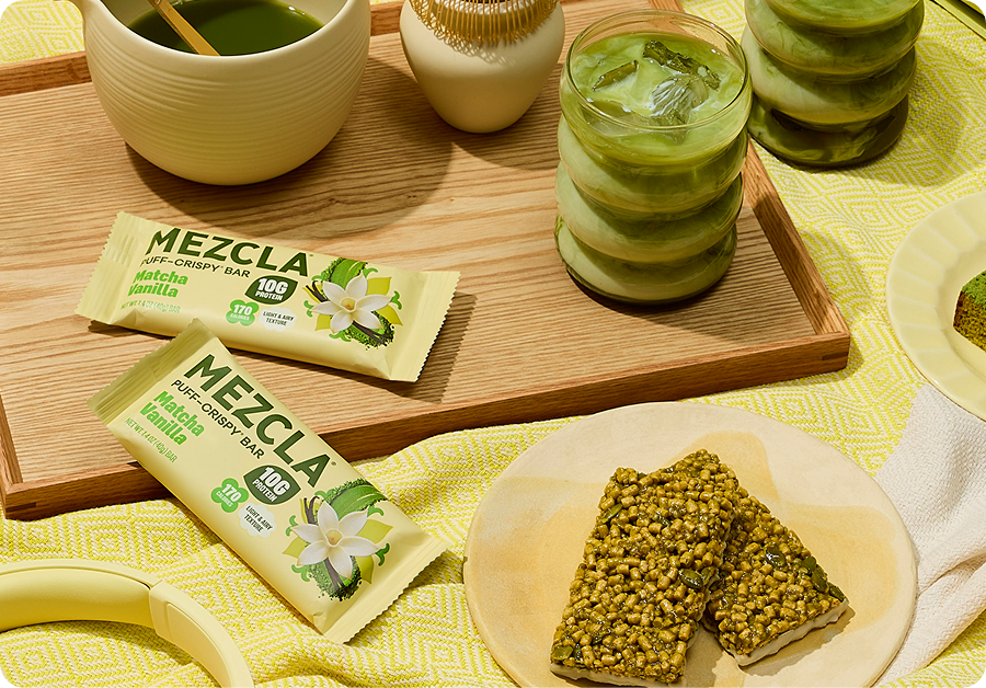 Mezcla matcha vanilla protein bars and green beverages arranged on wooden boards with yellow textiles, featuring natural ingredients and healthy snacks.