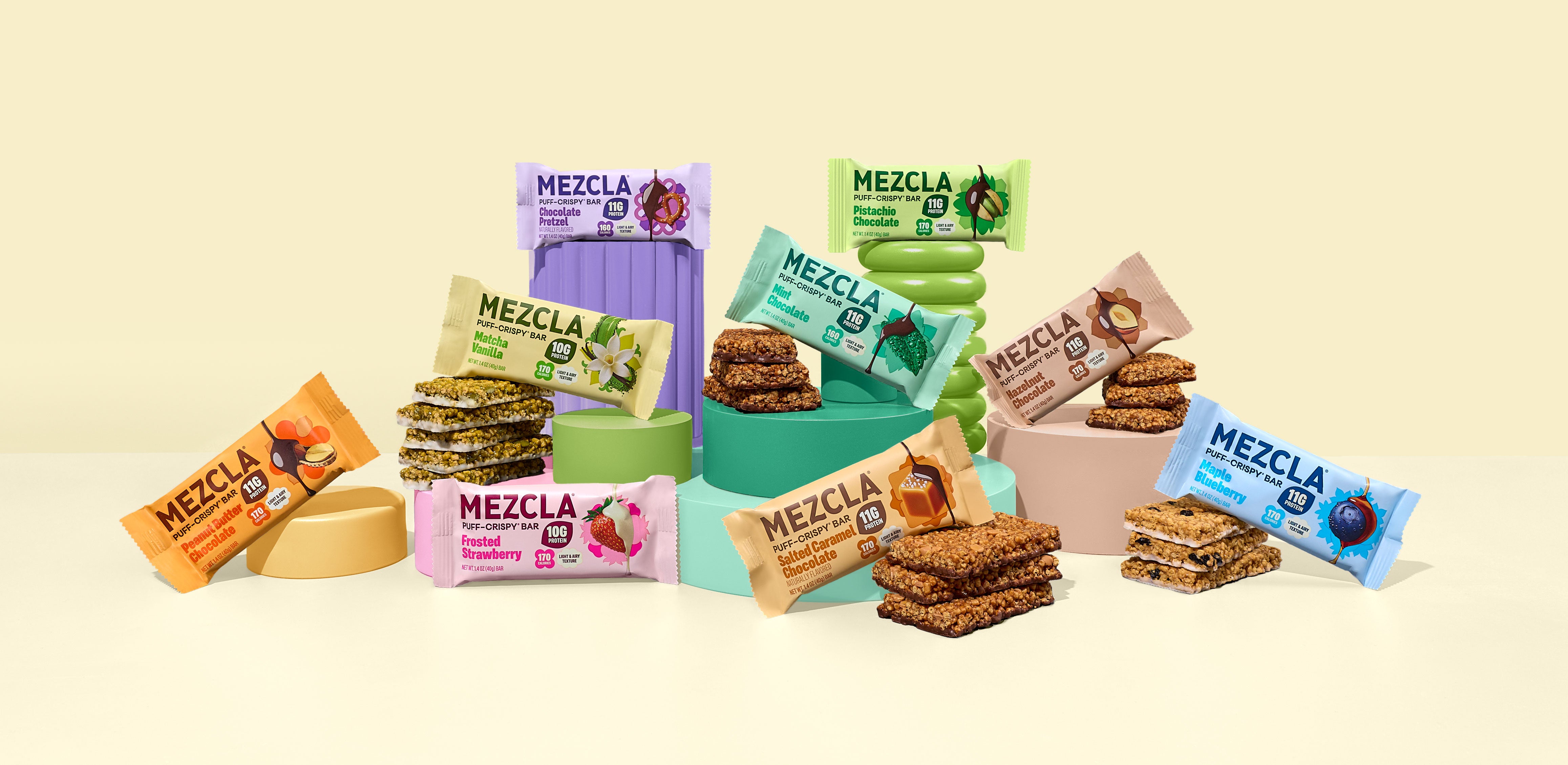 Colorful array of MEZCLA puff-crispy bars in various flavors including chocolate pretzel, pistachio vanilla, matcha, frosted strawberry, and blueberry, displayed with stacked bars and vibrant packaging