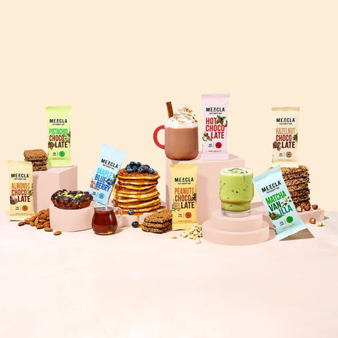 Colorful MEZCLA product lineup featuring various chocolate and matcha drink mixes with prepared beverages, pancakes, and snack bars on pastel platforms