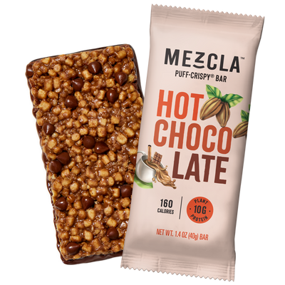 Mezcla Hot Chocolate puff-crispy protein bar in pink packaging next to unwrapped bar showing brown chocolate coating and mixed nuts on black background