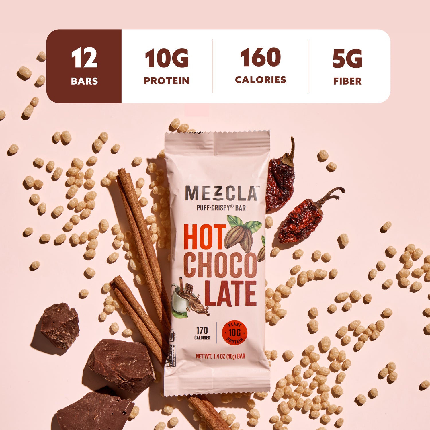 Mezcla Hot Chocolate protein bar package surrounded by scattered chickpeas, cinnamon sticks, chocolate chunks, and chili peppers on pink background with nutrition facts showing 12 bars, 10g protein, 160 calories, 5g fiber.