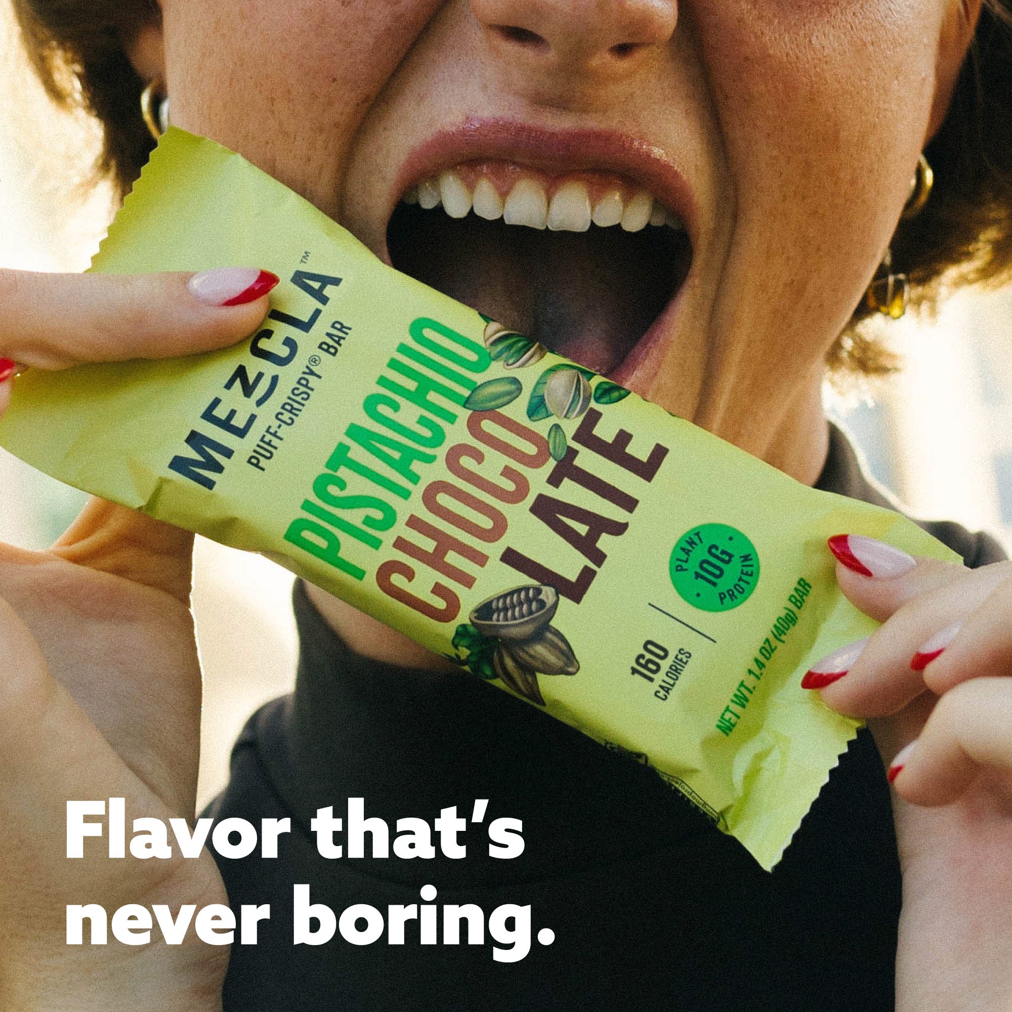 Woman with red nails holding green Mezcla Pistachio Chocolate protein bar package near her smiling mouth