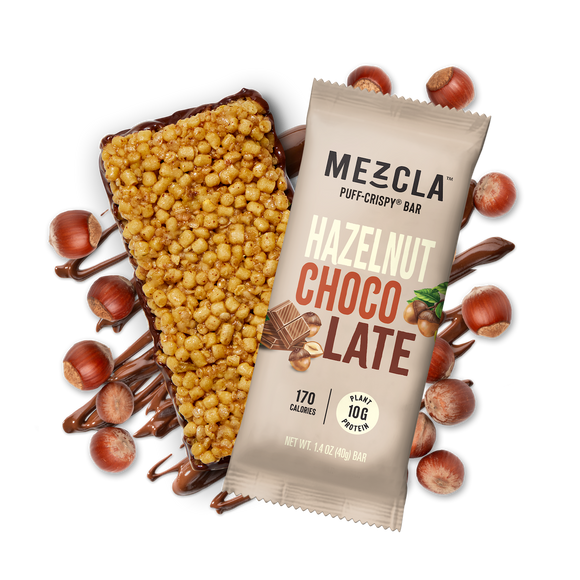 Mezcla Hazelnut Chocolate puff-crispy protein bar in tan package with unwrapped bar showing crispy texture, surrounded by hazelnuts and chocolate drizzle