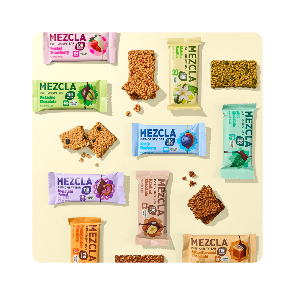 Various Mezcla puff-crispy protein bars in colorful packaging including Roasted Strawberry, Pistachio Chocolate, Maple Blueberry, Chocolate Pretzel, and Salted Caramel flavors arranged with unwrapped bars showing texture