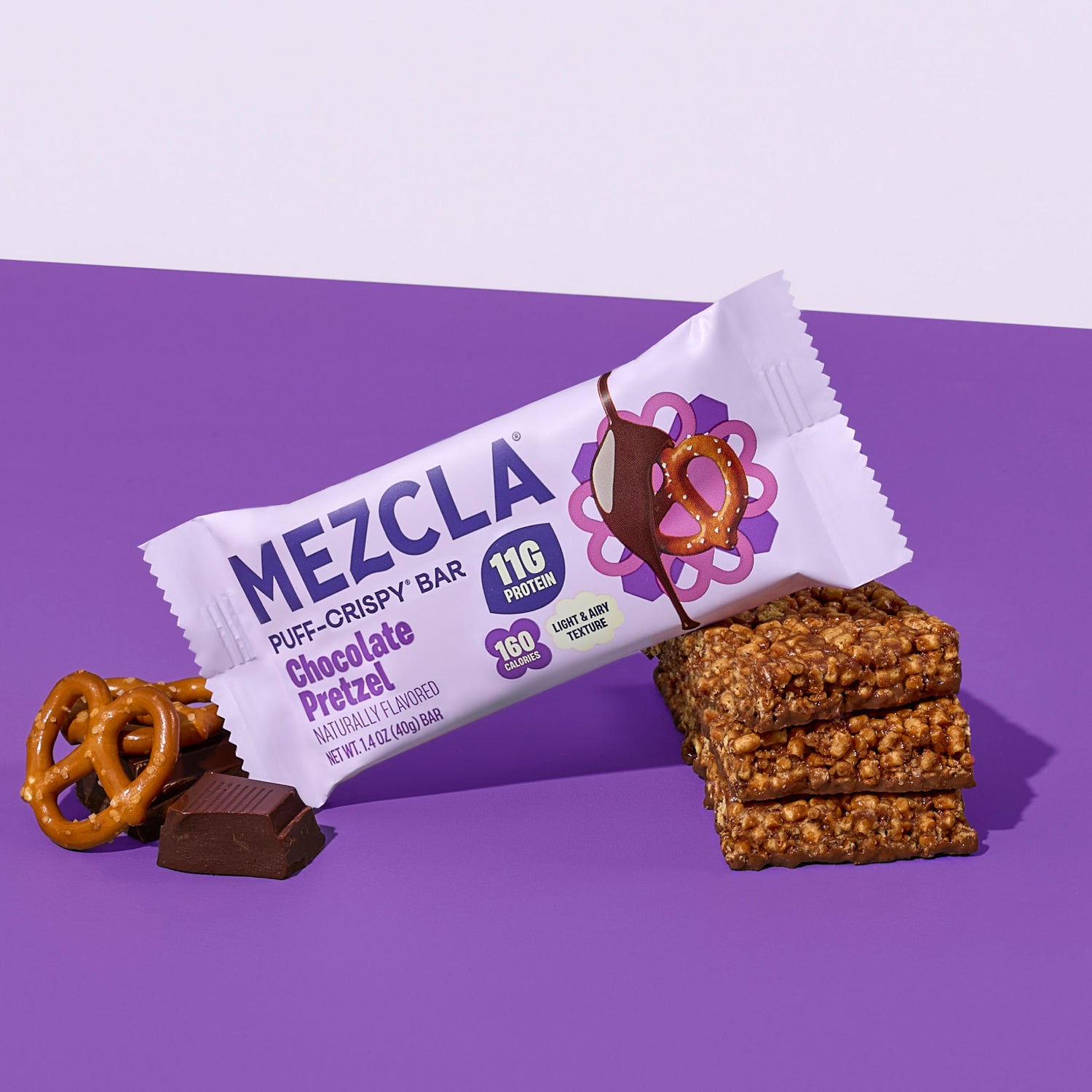 Mezcla Chocolate Pretzel protein bar package with pretzel pieces, chocolate squares, and stacked granola bars on purple background