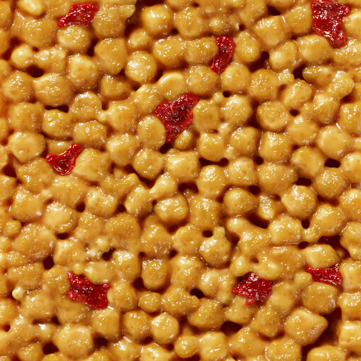 Golden caramel-coated cereal pieces mixed with red dried cranberries or cherries in a close-up view