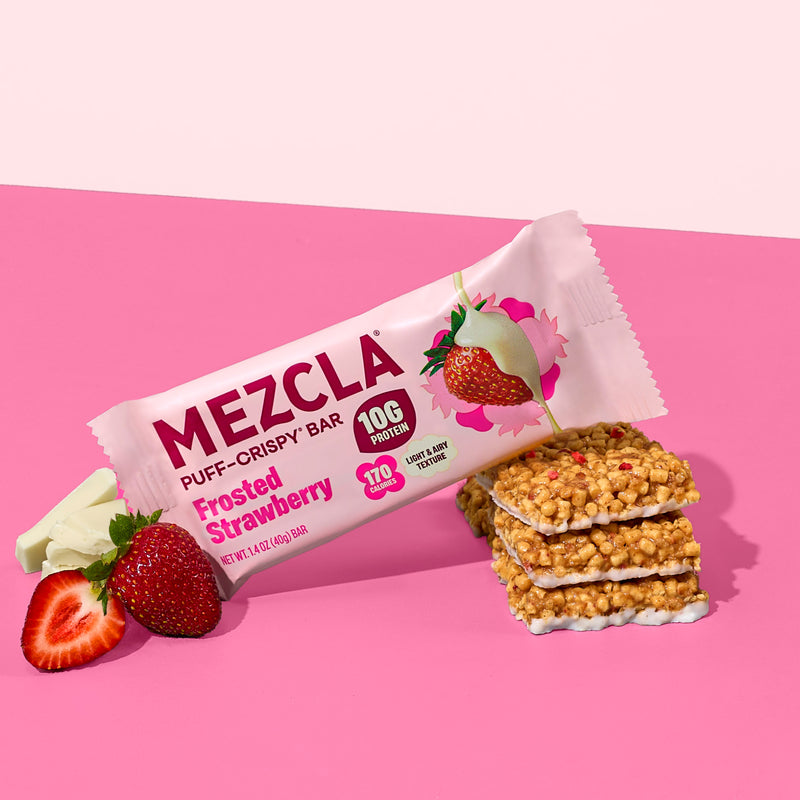 MEZCLA Frosted Strawberry puff-crispy protein bar package with 10G protein, 170 calories, alongside fresh strawberries and stacked bar pieces on pink background