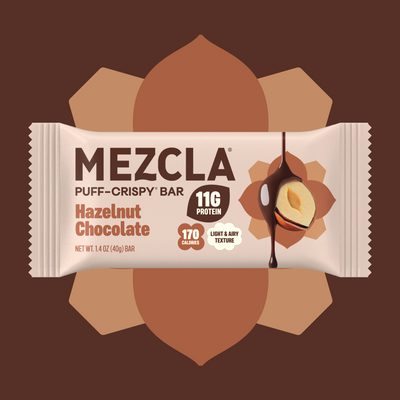 MEZCLA Hazelnut Chocolate puff-crispy protein bar package with 11G protein and 170 calories, featuring chocolate-dipped hazelnut graphic on brown geometric background.