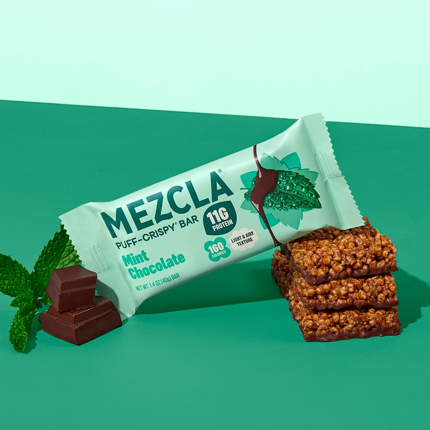 Mezcla Mint Chocolate puff-crispy protein bar package with 11g protein and 160 calories, displayed with chocolate pieces, mint leaves, and stacked bar pieces on green background