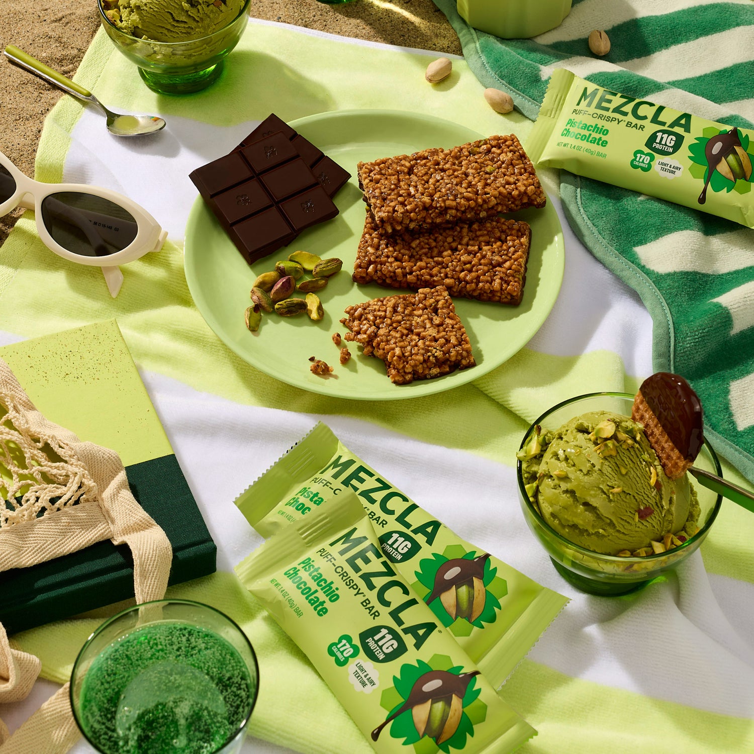 Green MEZCLA crispy bars with rice and chocolate displayed on lime green plate alongside dark chocolate squares, pistachios, and green ice cream in glass bowls on striped towel