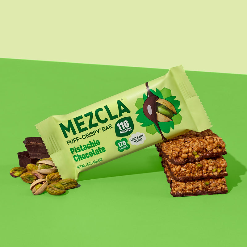 MEZCLA Pistachio Chocolate puff-crispy protein bar package on green background with pistachios and stacked bar pieces showing texture