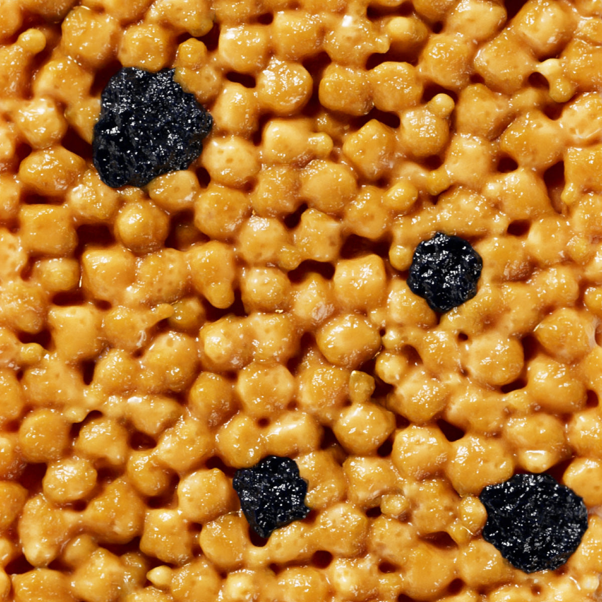 Golden crispy rice cereal with dark raisins scattered throughout, appearing glossy and caramelized