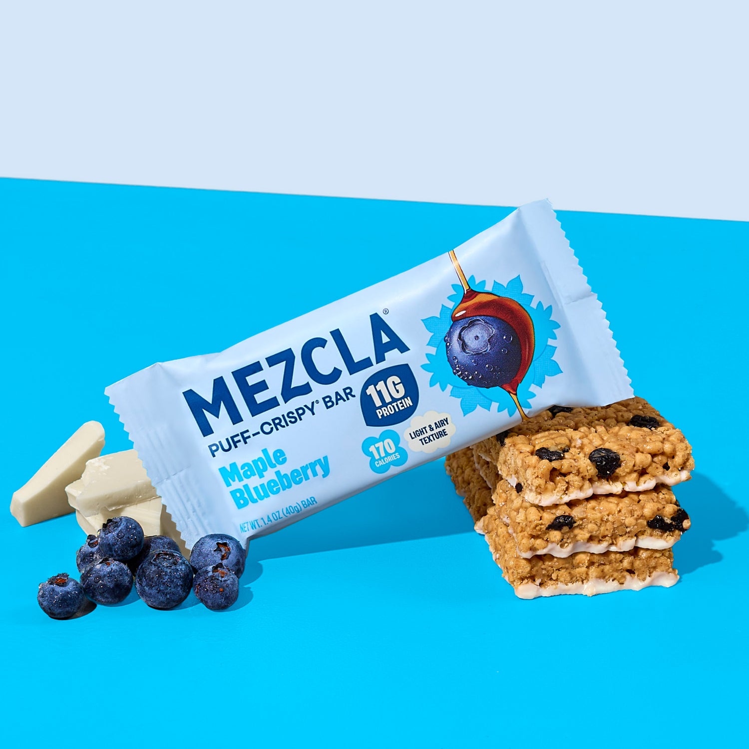 MEZCLA Maple Blueberry puff-crispy protein bar package with 11g protein and 170 calories, displayed with fresh blueberries and white chocolate pieces on blue background